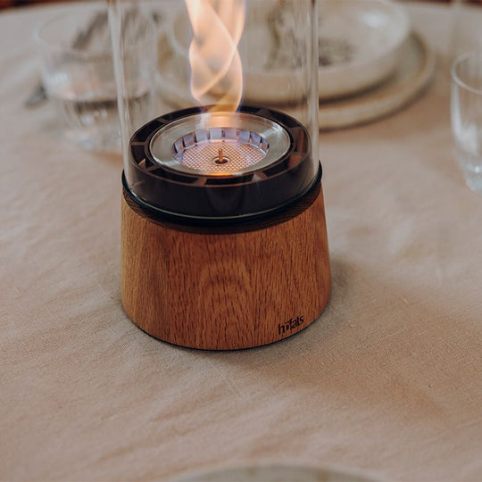 Lanterne design Höfats Spin Air 1200 en chêne allumée sur une table de terrasse en soirée. Feu d'ambiance décoratif sans fumée pour extérieur et intérieur.